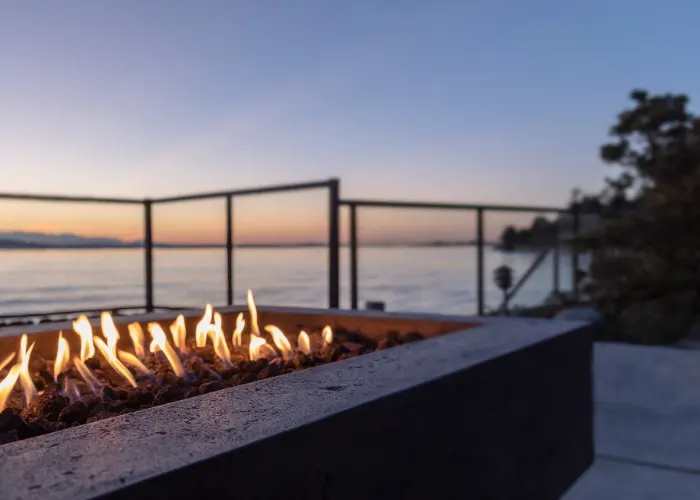 A steel gas firepit in a backyard on a lake